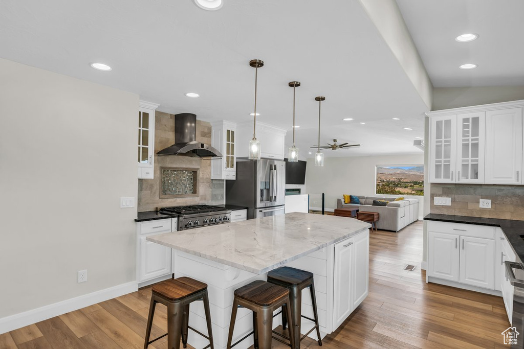 Kitchen featuring wall chimney exhaust hood, stainless steel fridge, backsplash, a center island, and white cabinets