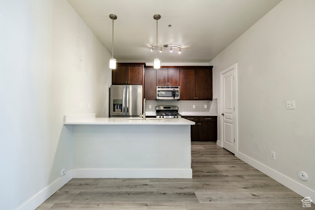 Kitchen featuring appliances with stainless steel finishes, dark brown cabinetry, decorative backsplash, light countertops, and a peninsula
