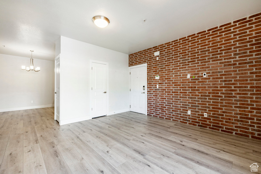 Empty room featuring a chandelier, brick wall, wood finished floors, and baseboards
