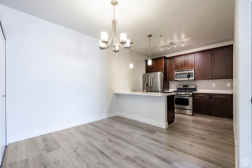 Kitchen featuring appliances with stainless steel finishes, dark brown cabinets, a chandelier, a peninsula, and light wood-style flooring