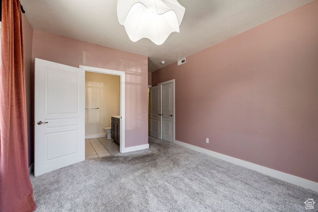 Unfurnished bedroom with light carpet, ensuite bathroom, and baseboards