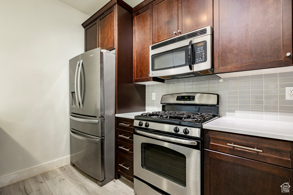 Kitchen featuring appliances with stainless steel finishes, light wood-type flooring, baseboards, and tasteful backsplash