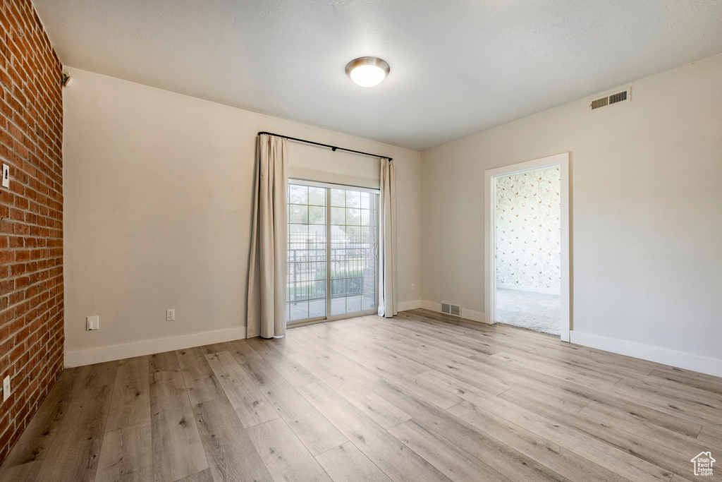 Unfurnished room with light wood finished floors, baseboards, and brick wall