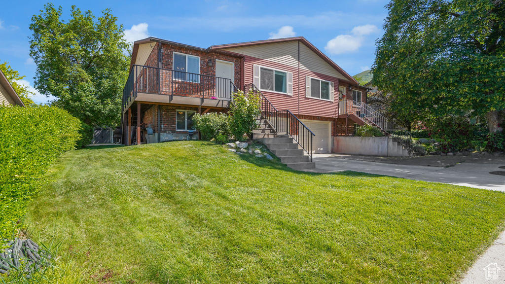 View of front facade with stairs, a garage, asphalt driveway, brick siding, and a front lawn