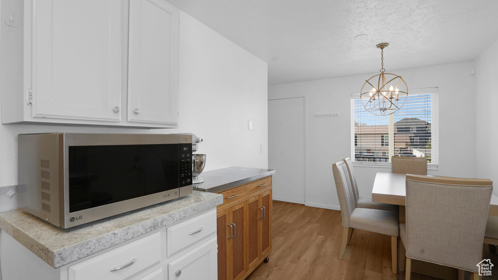 Kitchen featuring stainless steel microwave, a chandelier, light wood-type flooring, white cabinetry, and a textured ceiling