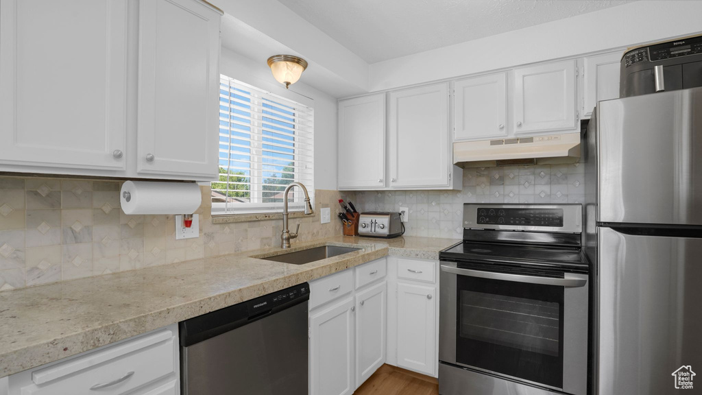 Kitchen featuring appliances with stainless steel finishes, a sink, under cabinet range hood, white cabinets, and backsplash