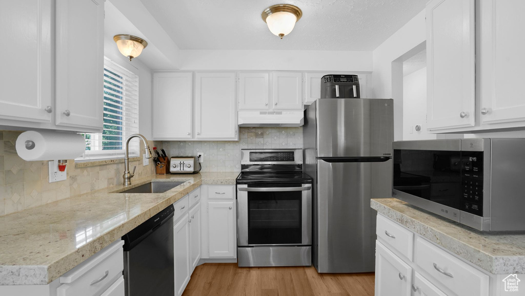Kitchen with appliances with stainless steel finishes, under cabinet range hood, a sink, white cabinetry, and decorative backsplash