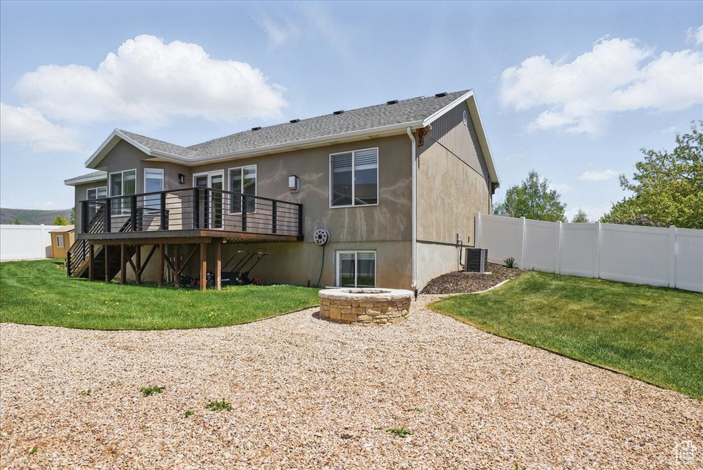 Rear view of property featuring cooling unit, a wooden deck, stucco siding, and a fire pit