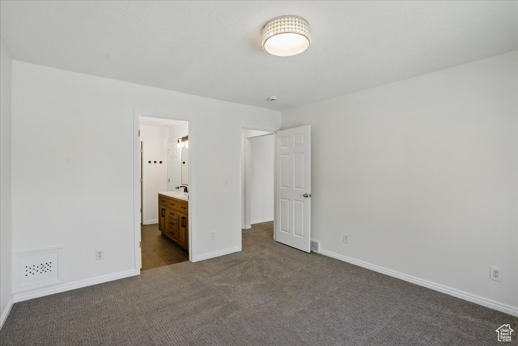 Unfurnished bedroom with dark colored carpet, baseboards, and connected bathroom