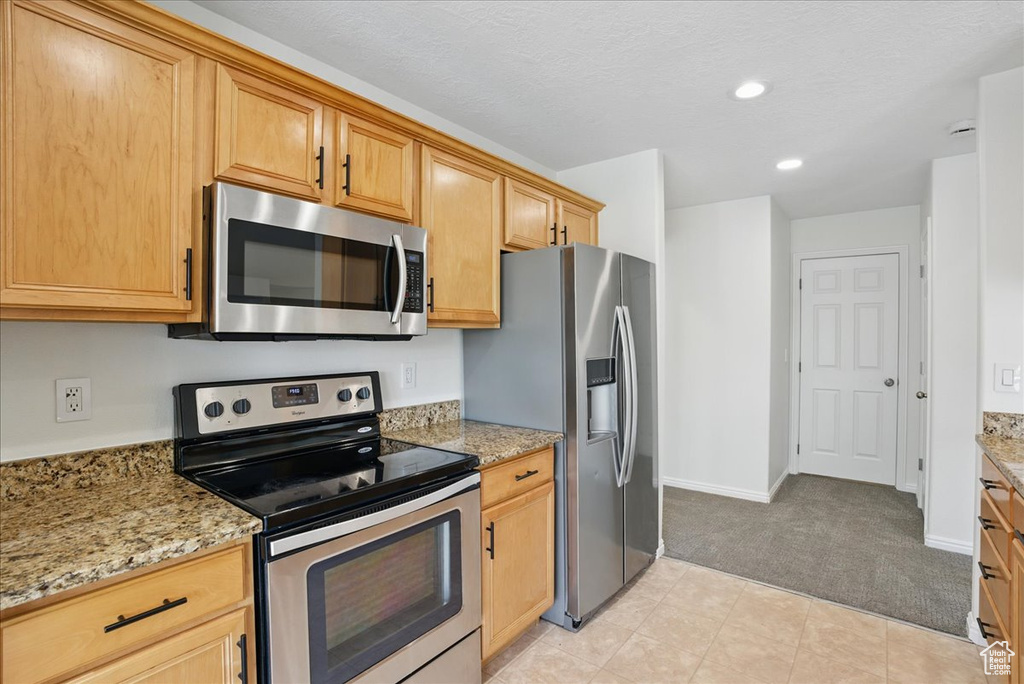 Kitchen featuring stainless steel appliances, light carpet, baseboards, recessed lighting, and light stone countertops