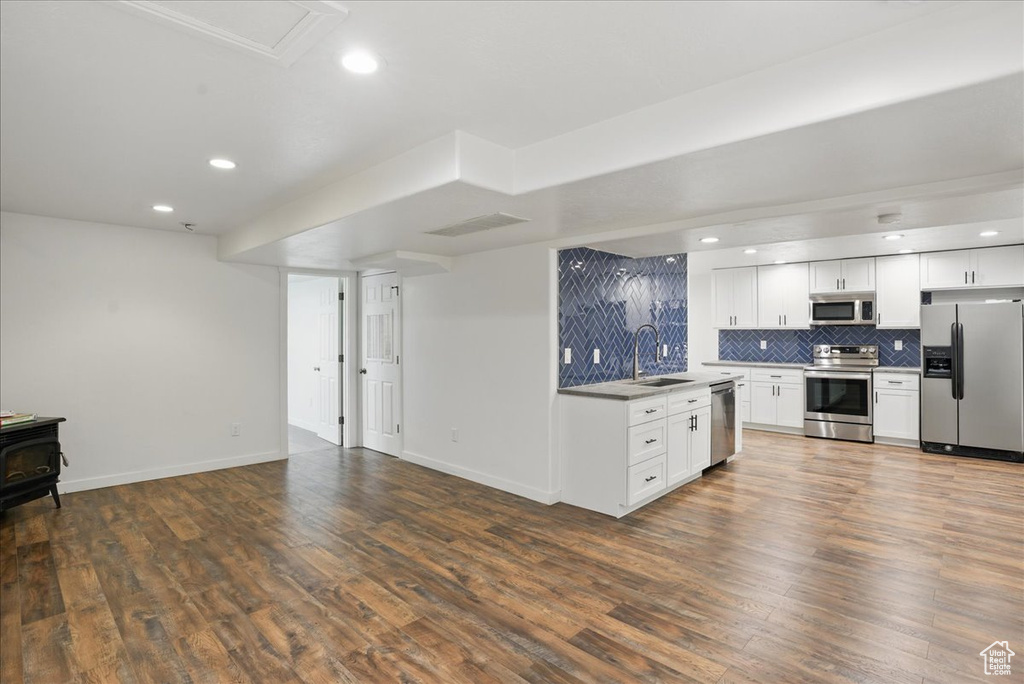 Kitchen with appliances with stainless steel finishes, a sink, open floor plan, decorative backsplash, and dark wood-type flooring