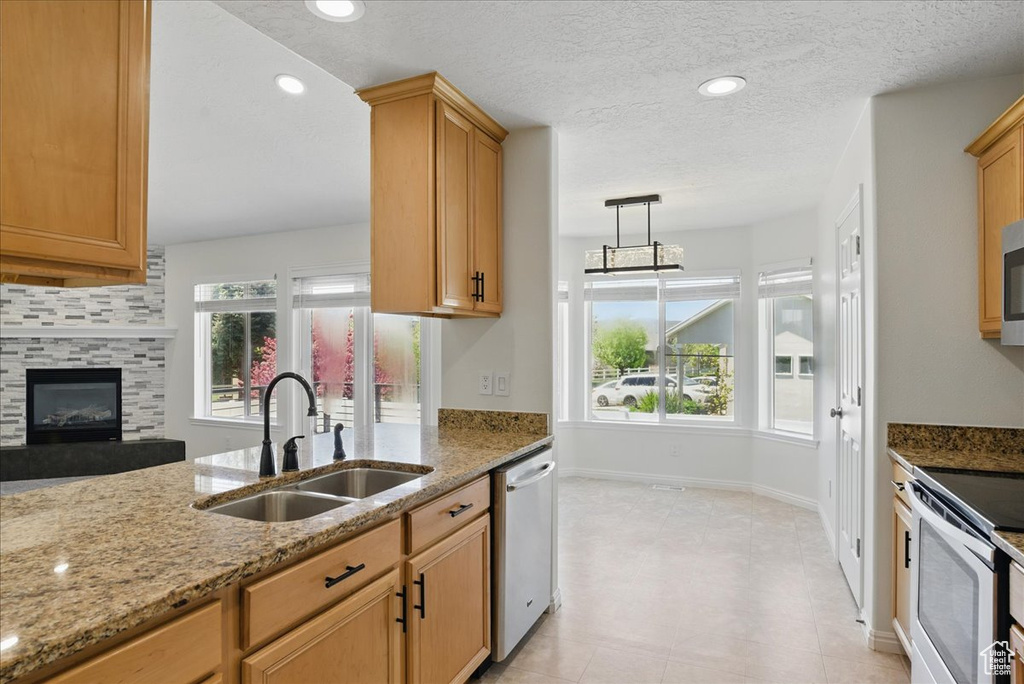 Kitchen with a sink, stainless steel dishwasher, light stone counters, electric range, and a fireplace
