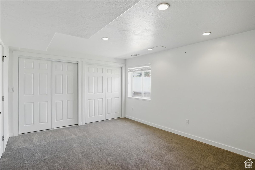 Unfurnished bedroom with carpet flooring, baseboards, recessed lighting, a textured ceiling, and multiple closets
