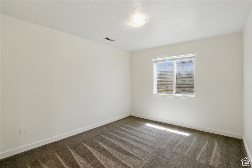 Empty room featuring dark carpet and baseboards