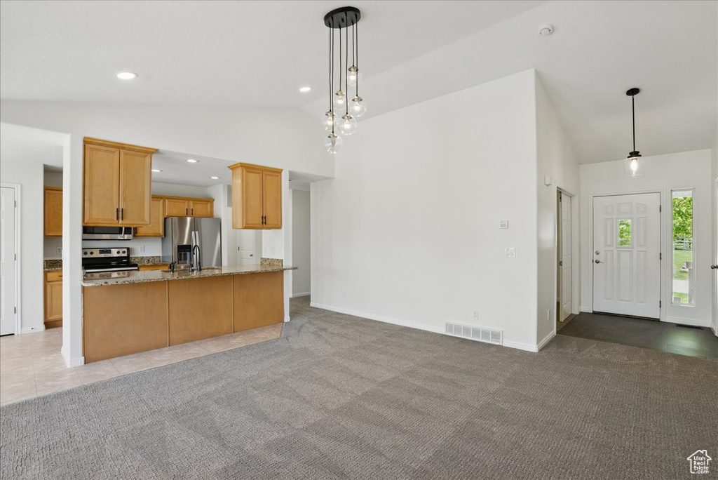 Kitchen featuring appliances with stainless steel finishes, light stone counters, open floor plan, light colored carpet, and high vaulted ceiling