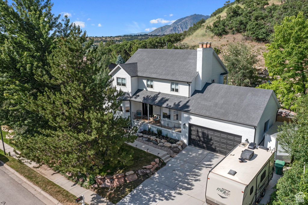 View of front facade featuring a chimney, a shingled roof, concrete driveway, an attached garage, and a mountain view