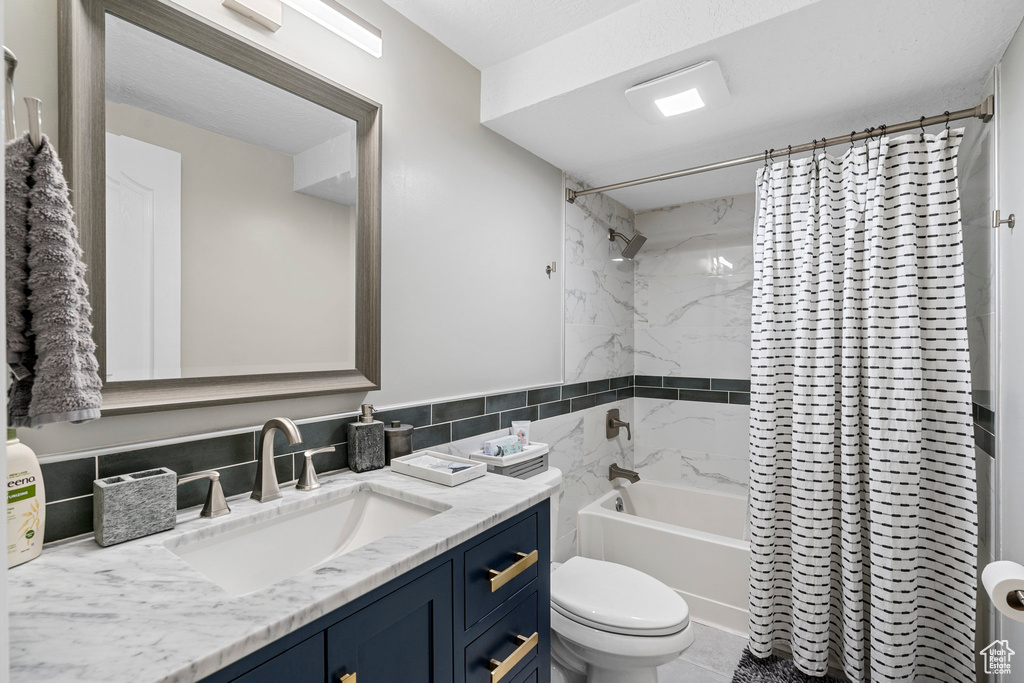 Bathroom with shower / bathtub combination with curtain, toilet, vanity, and tile walls