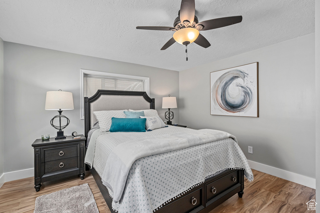 Bedroom with baseboards, a textured ceiling, wood finished floors, and a ceiling fan