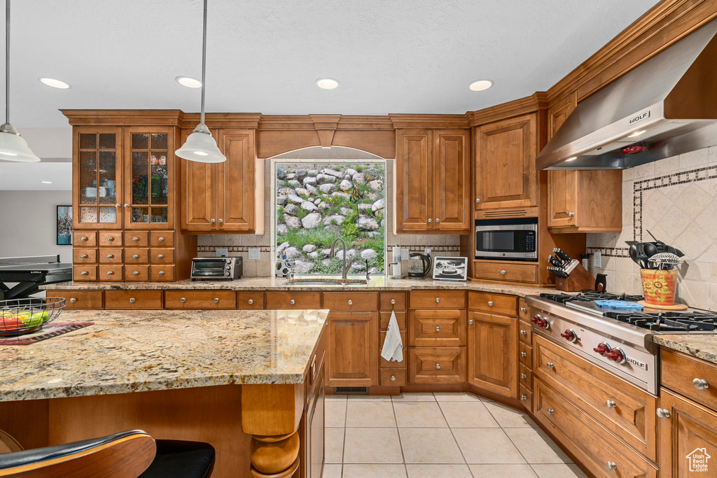 Kitchen with a sink, wall chimney exhaust hood, stainless steel appliances, tasteful backsplash, and brown cabinets