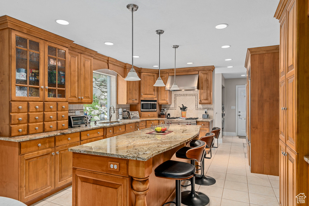 Kitchen featuring wall chimney exhaust hood, a sink, brown cabinets, light tile patterned floors, and a center island