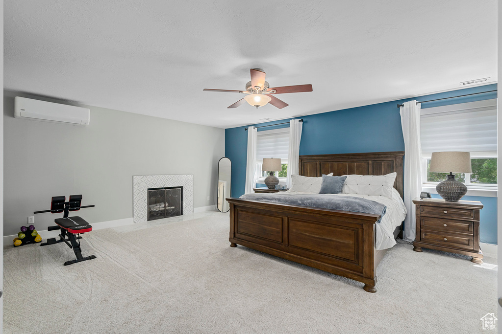 Bedroom with a wall mounted air conditioner, carpet, a fireplace, ceiling fan, and baseboards