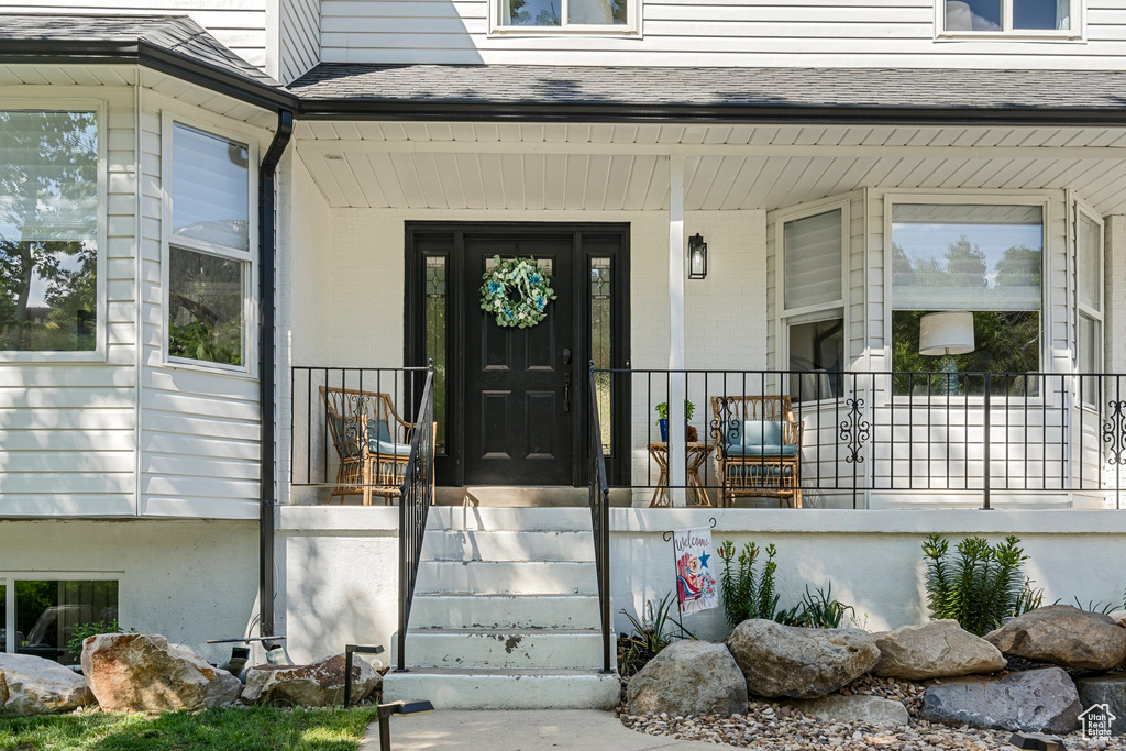 View of exterior entry with covered porch and a shingled roof