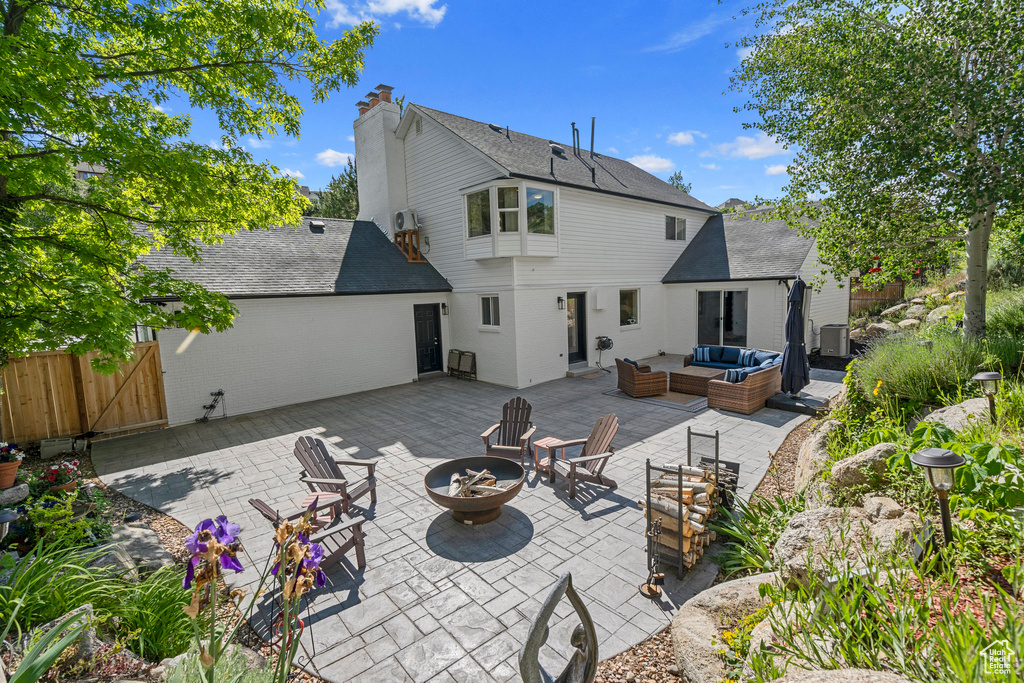 Back of house with an outdoor living space with a fire pit, a patio area, a shingled roof, brick siding, and a gate