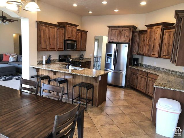 Kitchen with stainless steel appliances, a sink, a peninsula, ceiling fan, and light stone counters