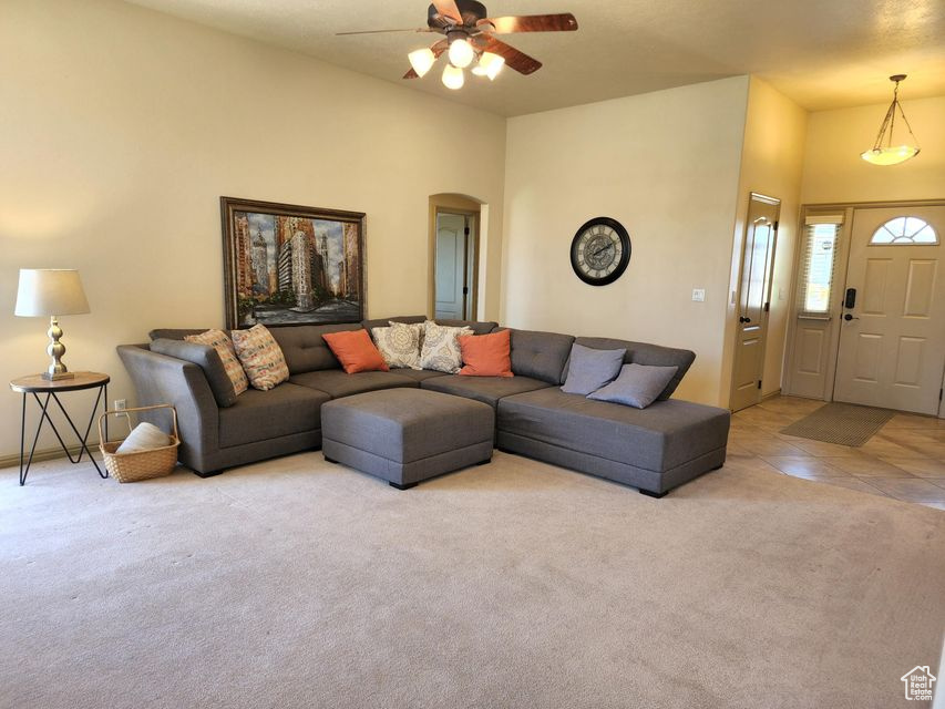 Carpeted living area with arched walkways, a ceiling fan, and tile patterned floors