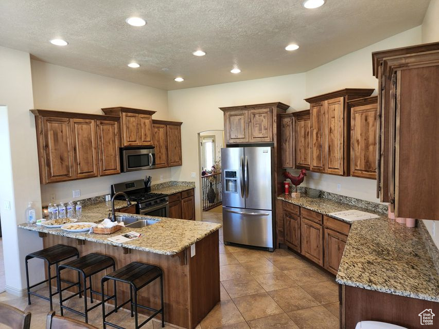 Kitchen featuring stainless steel appliances, a peninsula, a sink, a textured ceiling, and light stone counters