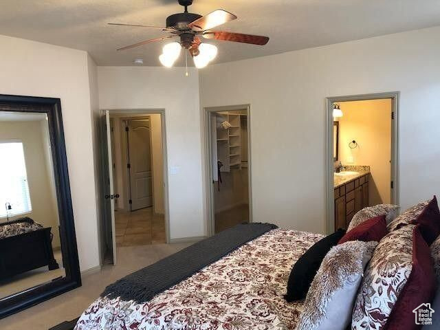 Bedroom featuring light carpet, a spacious closet, connected bathroom, ceiling fan, and a closet
