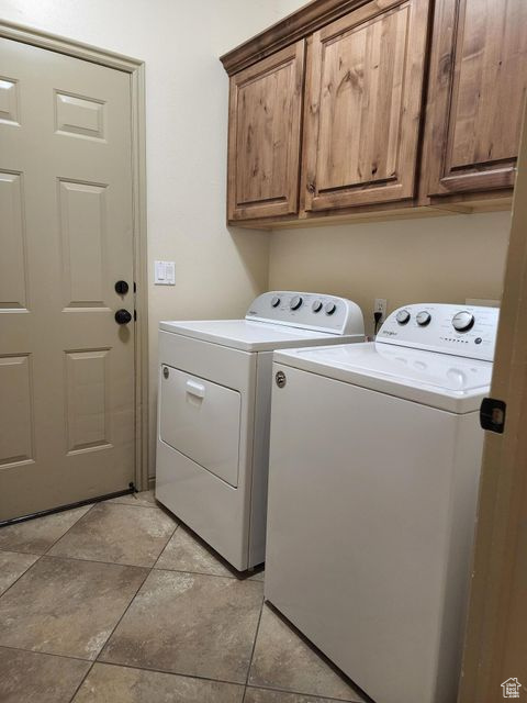 Washroom featuring washer and dryer, cabinet space, and light tile patterned flooring