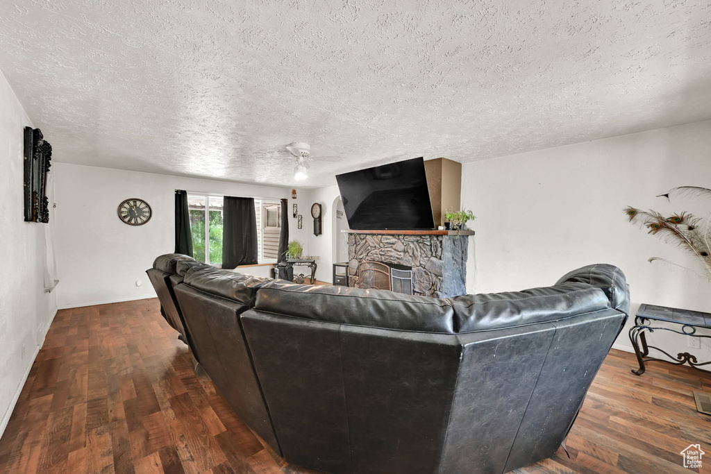 Living room with a textured ceiling, wood finished floors, and a stone fireplace