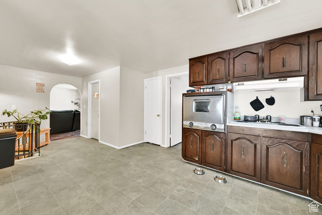 Kitchen featuring oven, under cabinet range hood, arched walkways, white stovetop, and dark brown cabinetry