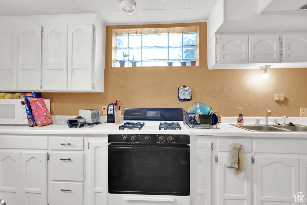 Kitchen featuring gas range, a sink, white cabinetry, and light countertops