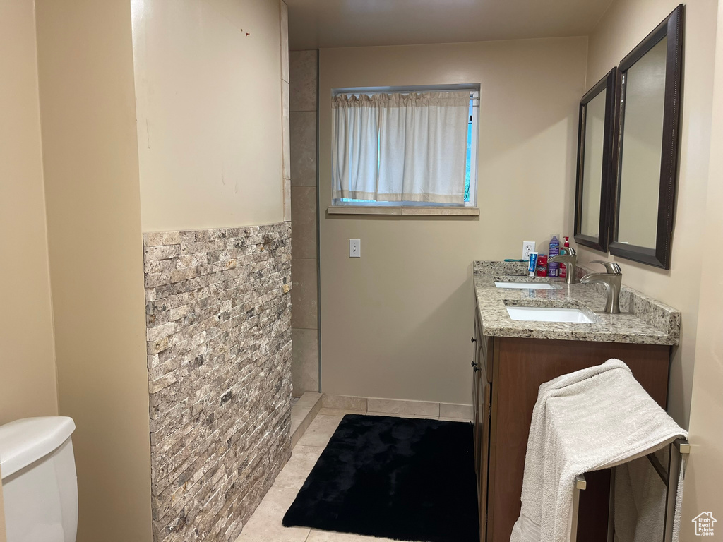 Bathroom featuring tile patterned floors, double vanity, toilet, and a tile shower