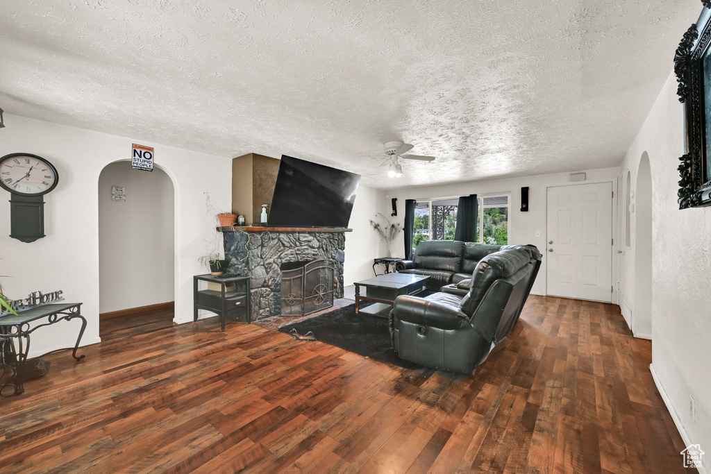 Living room featuring arched walkways, ceiling fan, a textured ceiling, wood-type flooring, and a fireplace