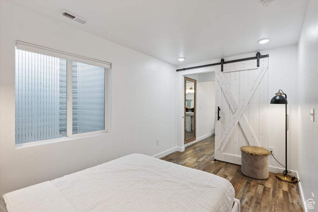 Bedroom with a barn door, wood finished floors, baseboards, and recessed lighting