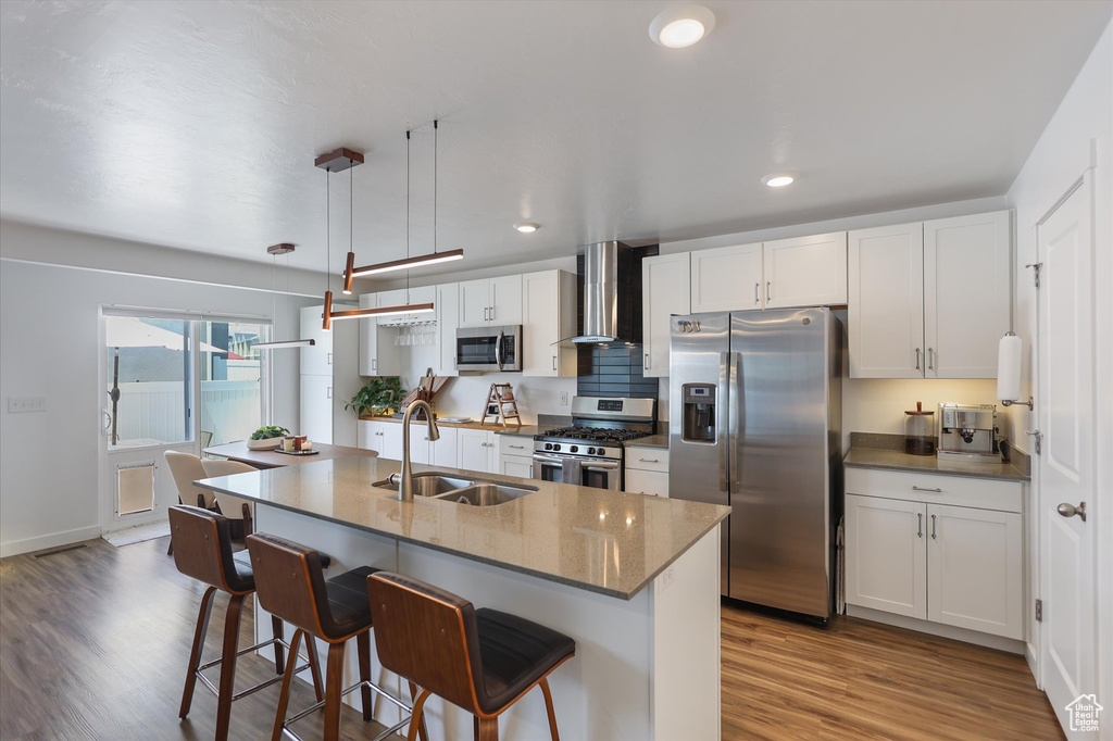 Kitchen featuring appliances with stainless steel finishes, wall chimney exhaust hood, a sink, a kitchen bar, and wood finished floors