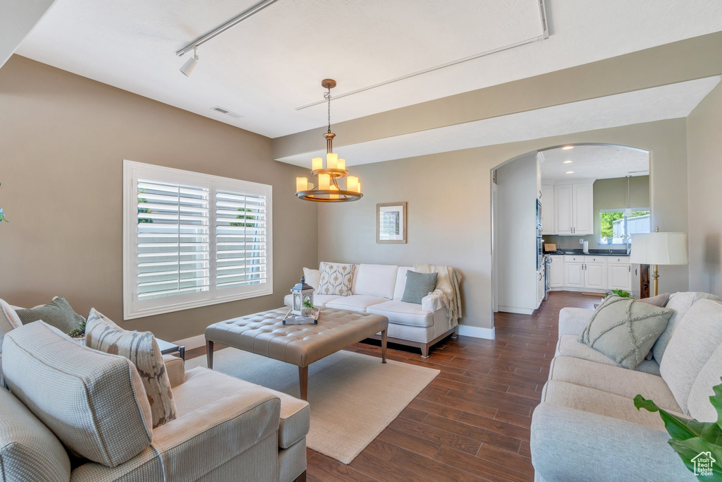 Living area featuring arched walkways, dark wood finished floors, baseboards, a chandelier, and track lighting