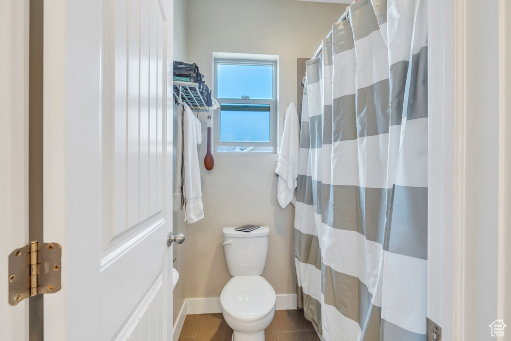 Bathroom featuring toilet, baseboards, a shower with shower curtain, and wood finished floors