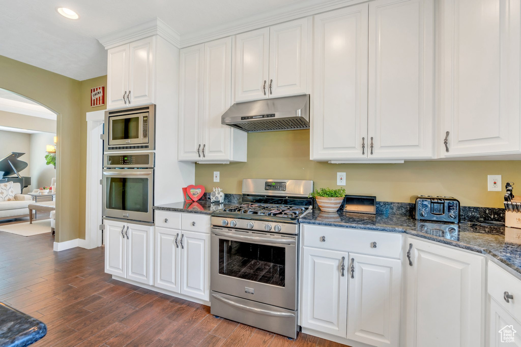 Kitchen with appliances with stainless steel finishes, under cabinet range hood, arched walkways, white cabinetry, and recessed lighting