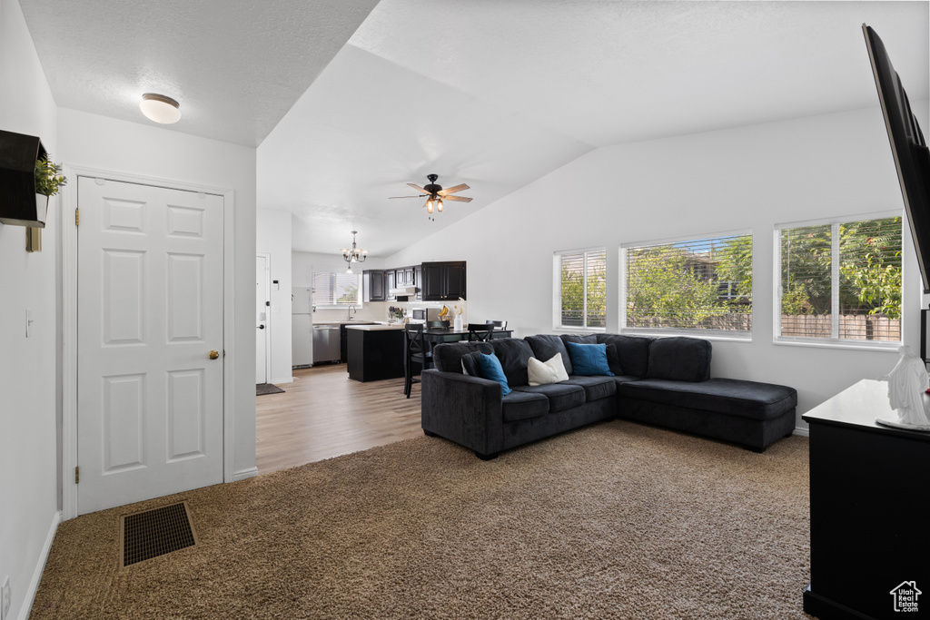 Living area with light colored carpet, vaulted ceiling, ceiling fan, and a chandelier