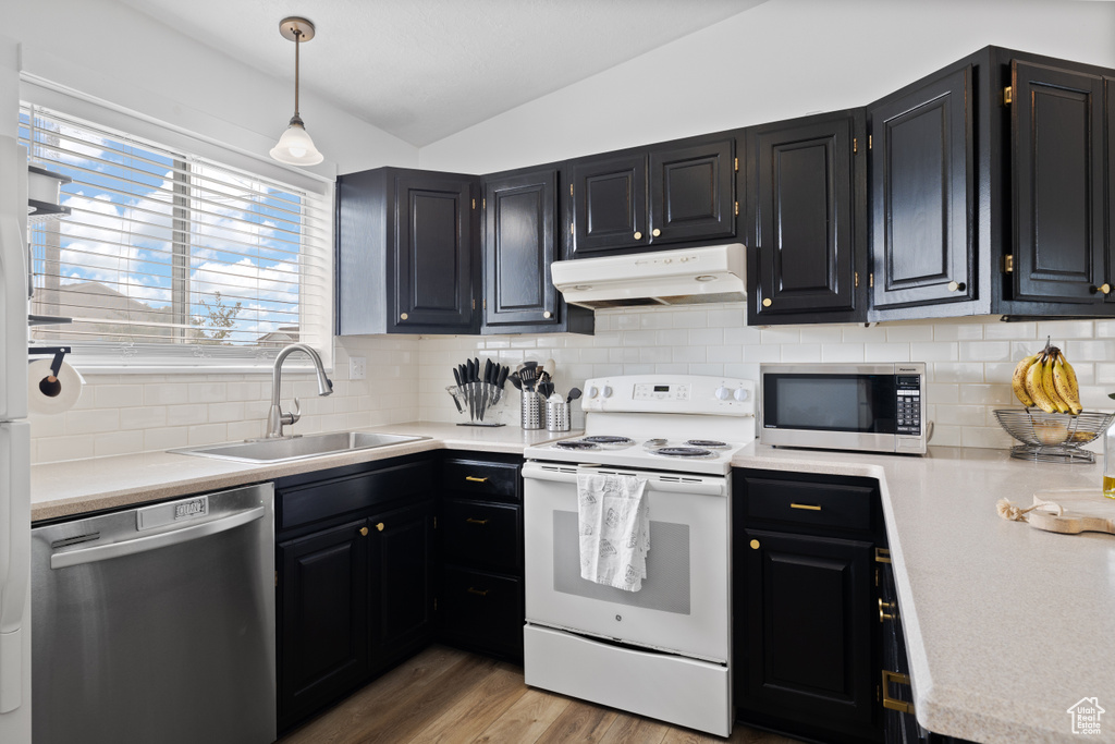 Kitchen featuring stainless steel appliances, a sink, vaulted ceiling, under cabinet range hood, and light countertops
