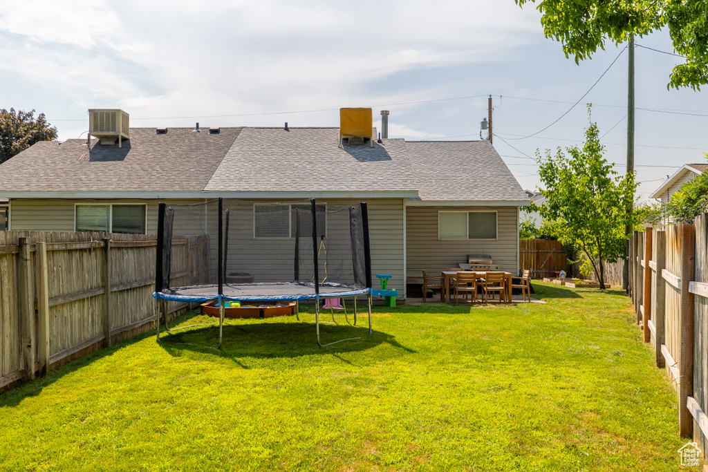 Rear view of house featuring a trampoline, roof with shingles, and central AC