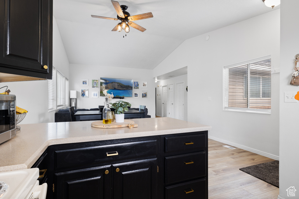 Kitchen with dark cabinetry, a peninsula, lofted ceiling, light wood-type flooring, and light countertops