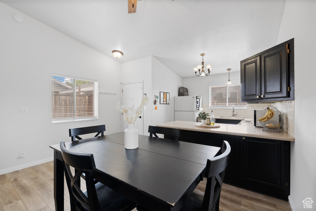 Dining room featuring a chandelier, light wood finished floors, plenty of natural light, lofted ceiling, and baseboards