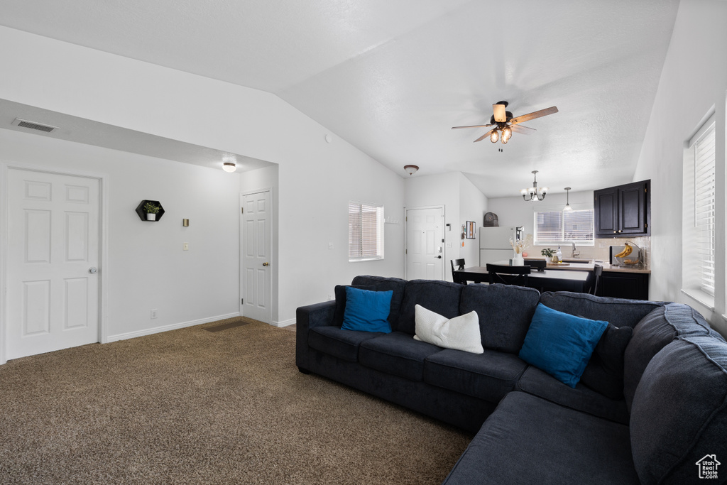 Living area with vaulted ceiling, carpet, a ceiling fan, a chandelier, and baseboards