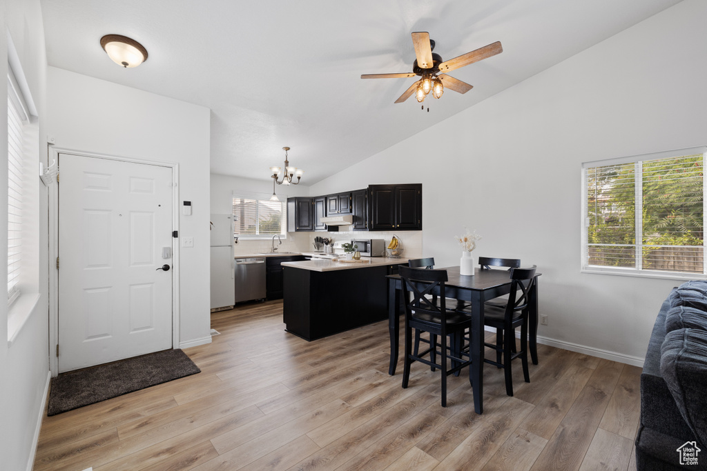 Dining area featuring a chandelier, vaulted ceiling, light wood-style flooring, ceiling fan, and baseboards