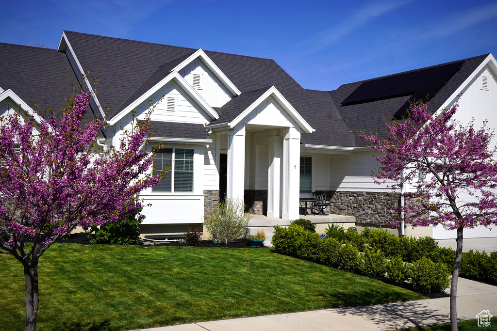 View of front of home featuring stone siding, a front yard, and roof with shingles